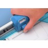 The image shows a hand holding a blue cutting tool with a level bubble, positioned near a ruler on paper. The tool is likely a rotary cutter or similar device used for precision cutting in crafting or design work.