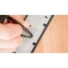 The image shows a hand using tweezers to pick up letters from a flat surface containing many small plastic letter tiles arranged in rows.