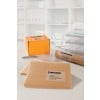 The image shows a workspace with an orange box, two brown envelopes, a rolled document, and a glass of water. All items are labeled with addresses related to a company named A&M Enterprise.