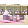 The image features various scented candles displayed on a table, with two prominent candles in glass holders labeled 'Lime & Bay' and 'White Lily' surrounded by gift boxes in shades of purple. The background shows additional candles organized on a shelf.