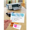 The image shows a printer on a tabletop with business cards and a customer card for a hairstyling service. The customer's card displays the name Neumeier, Brigitte, with contact information. Other cards on the table are for Just Nails and The Coffee Pot.