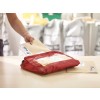 The image shows a person holding a beige envelope and placing it next to a red bag on a table. In the background, there are several bags, possibly containing supplies.