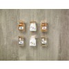 The image contains six glass jars on a textured surface. The jars are labeled with spices and ingredients: coffee, salt, flour, pepper, and other seasonings. Each jar has a cork lid and is arranged in two rows.