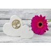 The image shows two white wooden hearts, one of which is decorated with a golden tree in a circle. Next to it, there is a pink flower on a wooden background.