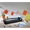 The image shows a crafting workspace with a paper cutter, colored sheets, scissors, paper clips, and a potted plant. The colored sheets are hung with clothespins on a string.