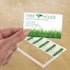 The image shows a hand holding a business card for 'TREE HOUSE', an agency focused on environmental protection. The card features a green grass design and includes contact information for the agency.