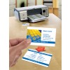 The image shows a printer with business cards printed next to it. A business card is in hand, highlighting contact information for 'Solutions IT' in London, Berlin, and Paris. A yellow keyboard is also visible.