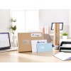 The image shows a workspace with a laptop, a large cardboard box, various letters, a cylindrical package, and an organized filing tray, all of which are labeled with addresses.