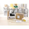The image shows a packing station with a labeling printer, various sizes of envelopes, a package, and rolls of packing material, all arranged on a table. Background contains bags likely used for storage.