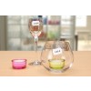 The image features a table setting with three items: a wine glass with a price tag of 2,95 €, a pink candle in a glass holder, and a larger glass bowl with a green candle and a price tag of 3,95 €. The background is blurred, emphasizing the foreground items.