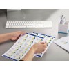 The image shows a person's hand holding a sheet of labels that feature a logo and names. There is a keyboard and a container with pens in the background, indicating a workspace.