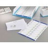 The image shows a modern desk setup with a keyboard, a stack of laminated contact labels, and a tray with an envelope. The labels and envelope have a logo with an abstract triangle and are designed for professional correspondence.