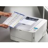An individual is holding a sheet of printed labels in front of a laser printer. The printer is printing another document, and the labels feature a design with colored triangles and text.