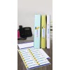 The image displays three binders labeled 'Budgets,' 'Marketing,' and 'Meetings' arranged on a wooden desk. In front of them, there's a sheet of labels featuring the same titles along with 'Customers.' A black telephone is visible in the background.