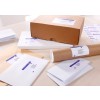 The image displays various packaging materials on a table, including a brown box, several envelopes of different sizes, a rolled document, and a stack of labels with addresses. The items all have printed labels, indicating they are prepared for mailing.