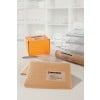 The image shows various shipping boxes and envelopes with labels. They are placed on a desk with a piece of paper and a glass of water in the background. The whole setup is organized and professional.