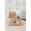 The image shows some brown shipping packages, including a box, envelope, and a tube, all labeled with 'Morena Consulting'. They are placed on a desk with a pen, a glass of water, and a background of organized documents.