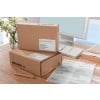 The image shows gifts in brown boxes with shipping labels, a pen and a computer on a desk with a vase of flowers in the background.