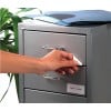 In the image, a hand is seen opening a drawer of a gray cabinet. The cabinet has a label indicating 'April - June' and there are some folders on top. A plant is visible on the side.