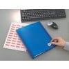 The image shows a blue folder on a desk with a hand attaching a label with the word 'TEMPORARY!'. There is a sheet of paper next to it with repeated text 'TEMPORARY!'. A keyboard and a mouse are visible in the background.