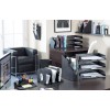The image shows a modern office space with a black leather chair, a desk organized with various filing and stationery supplies, and a window letting in natural light. Items include magazine holders, document trays, pens, and a computer monitor displaying a webpage.