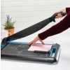 Image of a person using a paper cutter, placed on a table with a plant and a cup of coffee in the background.