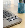 The image shows a laptop with a label indicating it is the property of PP Publications, alongside a blue pen holder filled with pens. The background appears to be an office environment.