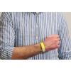 The image shows a close-up of a person's arm wearing a yellow wristband. The person is dressed in a blue and white striped shirt, with the arm positioned to show the wristband clearly.