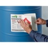 A person places a safety label with information about a polyurethane coating on a blue barrel. The label contains warnings and usage instructions.