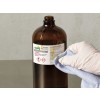 The image shows a brown glass bottle labeled with 'Ferric Chloride Solution 0.1M' and a warning about potential hazards. A hand wearing a glove is cleaning the bottle with a cloth.