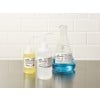 The image shows three containers on a countertop: two small bottles with yellow and clear liquids and a larger flask with blue liquid. Each container has warning labels indicating caution.