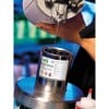 In the image, a liquid is being poured from a container. A hand holds a spray gun above a can that says 'Polyurethane Coating', with warning symbols. It looks like a paint or coating process.